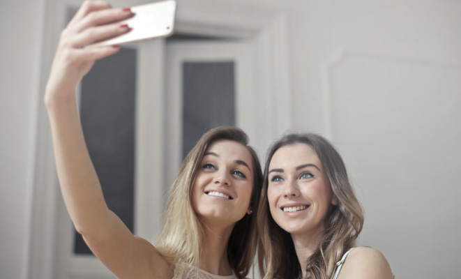 two young women with dirty blonde hair taking a selfie with a phone