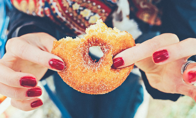 Closeup of a woman with fingernails painted red holding a donut covered in cinnamon sugar with a few bites eaten