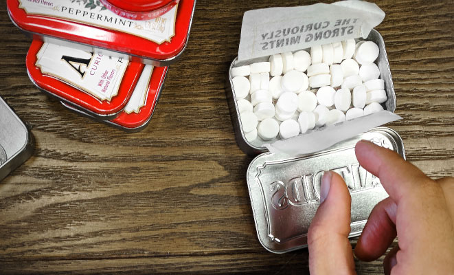 Aerial view of a hand reaching into a tin of peppermint Altoids breath mints on a wooden table