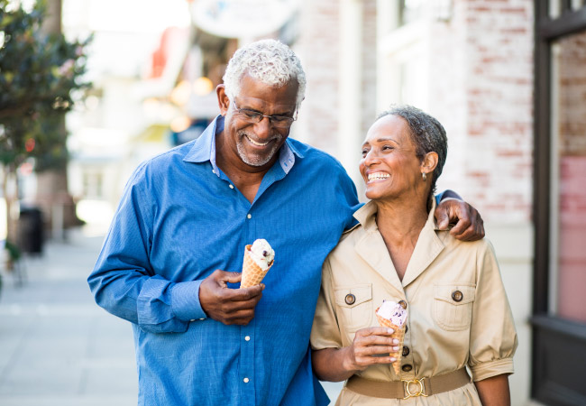 Husband and wife smile with dental implants as they walk down the sidewalk with ice cream cones